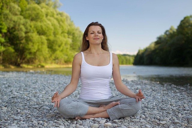 A lady meditates alongside a river.