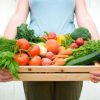 All local and organically grown fruits & vegetables in wooden vegetable crate held by a woman. Shallow dof, crisp focus across all the vegetables. Crate contains: peaches, green apple, peppers, green beans, rondelle carrots, baby carrots, zucchini squash, tomatoes, basil, fennel, kale, lettuce, broccoli, potatoes and radishes.