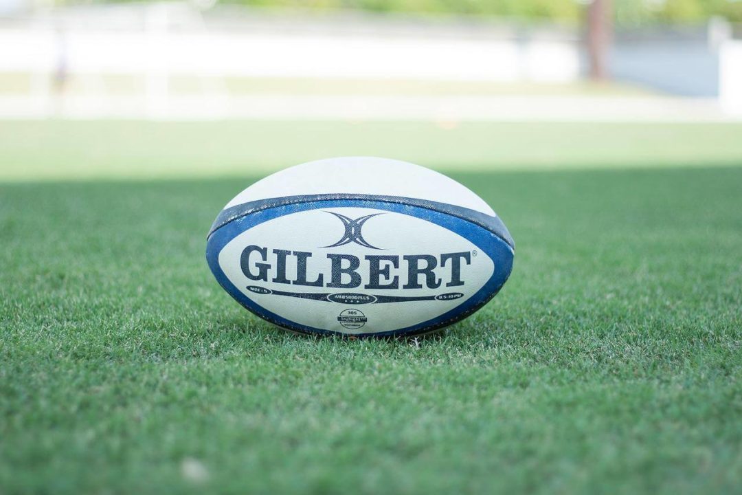 A white rugby ball lays on the green grass of a rugby pitch.