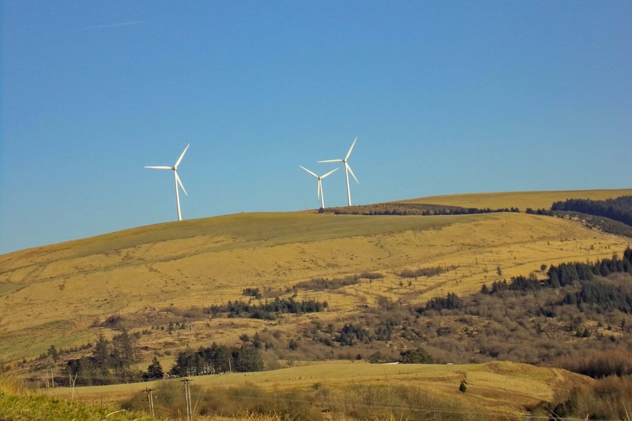 Wind turbines are on top of a hillside.